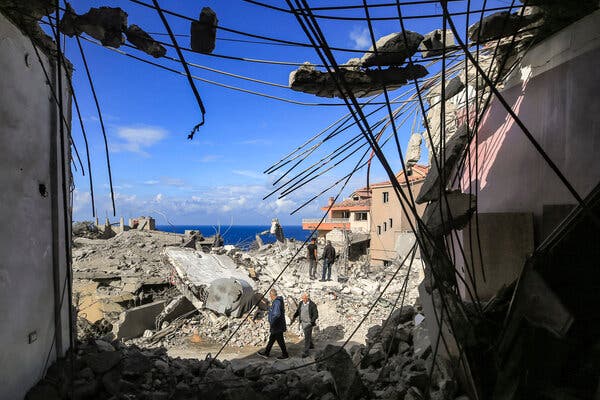 People walk amid rubble near badly damaged buildings, one with exposed metal rods.