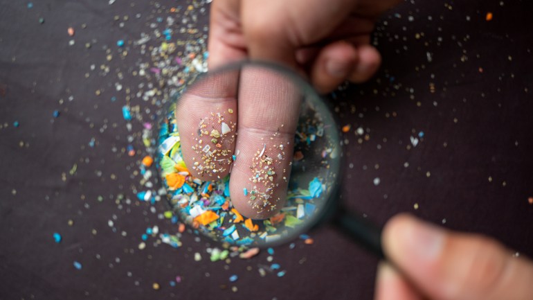 Close-up of micro plastic particles on the fingers under a magnifying glass. Concept for water pollution and global warming. Macro shot on a bunch of microplastics that cannot be recycled