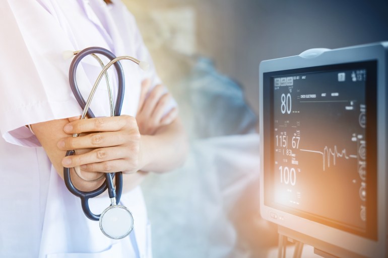 Doctor hold stethoscope in hand with electrocardiogram monitor in hospital surgery operating emergency room showing patient heart rate, medical rescue concept.