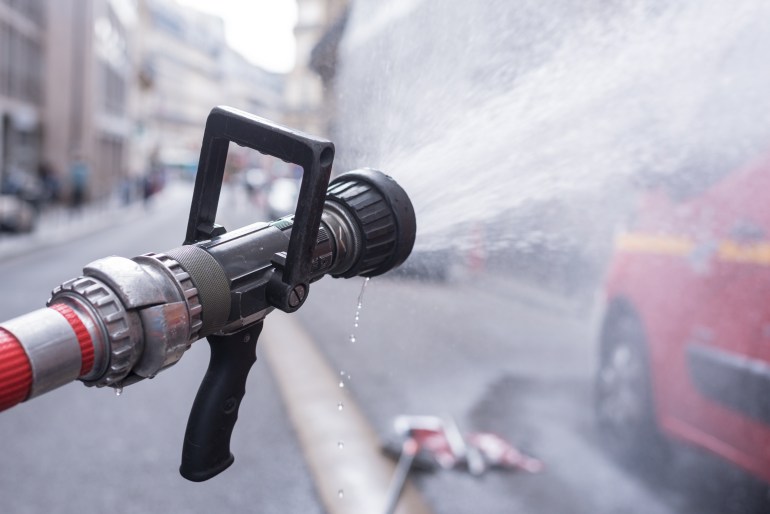 Water jet splashing from a fire fighting firehose nozzle with a red fire fighter truck in Paris