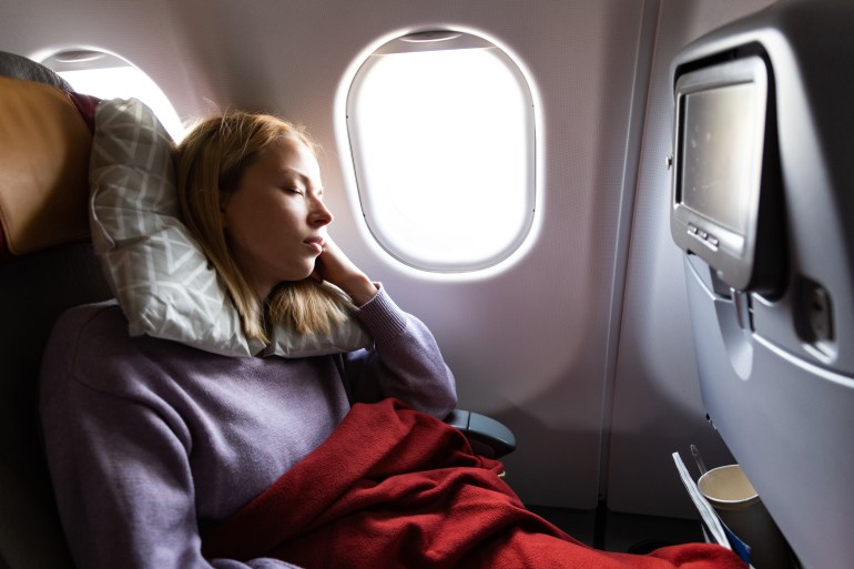 Tired blonde casual caucasian woman sleeping on seat while traveling by airplane on long distance transatlantic ...