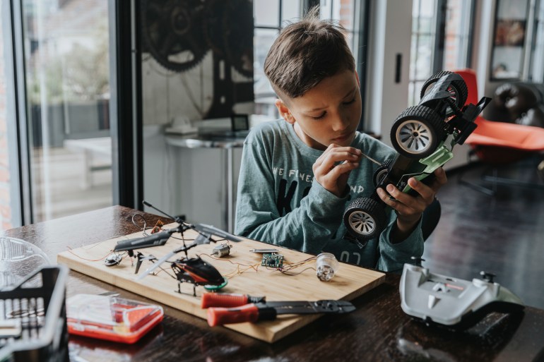 Boy tinkering on radio-controlled car with screwdriver and wires, Wuppertal, NRW, Germany