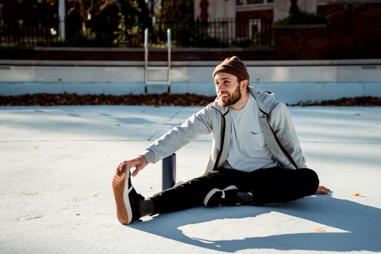 Smiling sportsman stretching leg on urban pavement