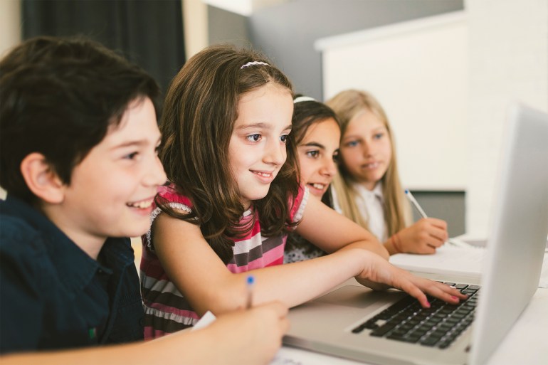 Children at coding class, sitting by the desk and using laptop. They are focused on their work, finishing their assignment.