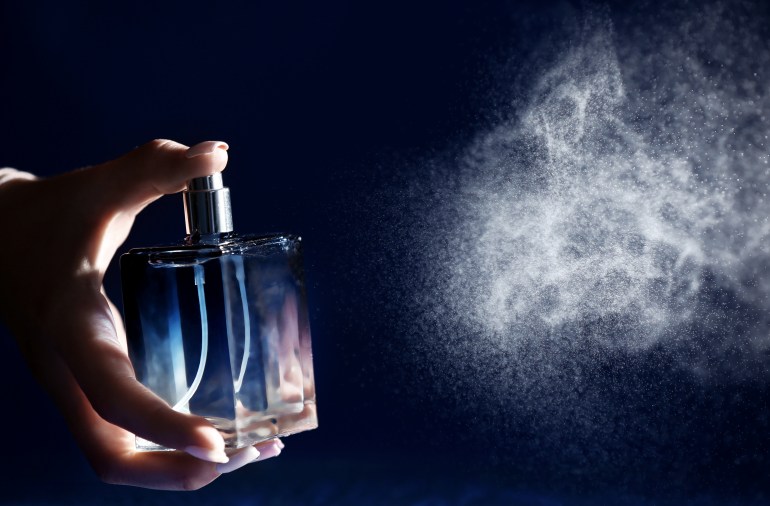 Woman spraying perfume on dark background, closeup