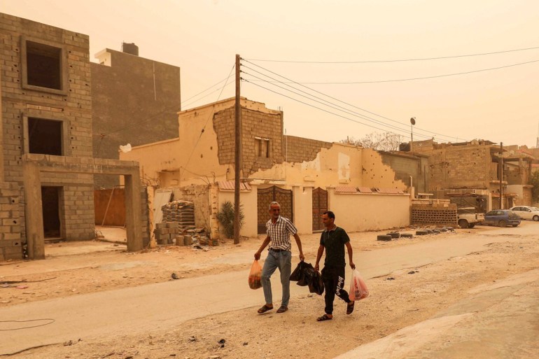 Two men walk with bags of produce along a street during a sandstorm in Libya's eastern city of Benghazi on April 22, 2024. (Photo by Abdullah DOMA / AFP)